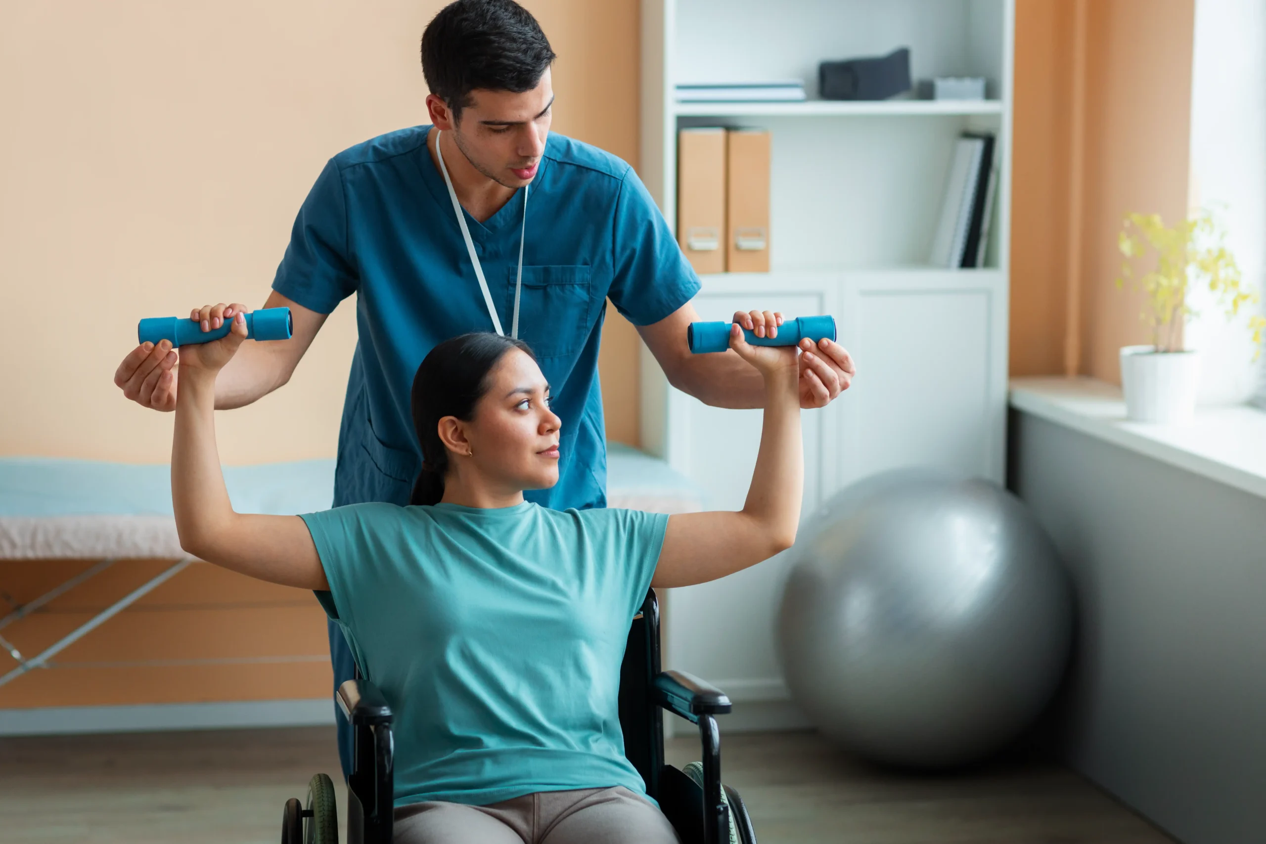 A healthcare professional assists a woman in a wheelchair lifting dumbbells, promoting strength training and rehabilitation. Bright, supportive atmosphere.