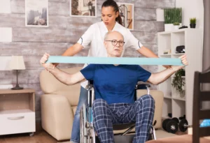 A caregiver assists an elderly man in a wheelchair with resistance band exercises in a cozy living room, conveying support and determination.