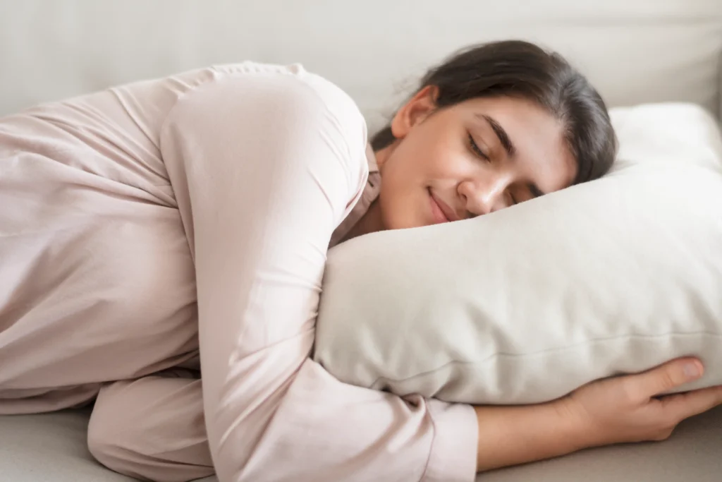 A woman peacefully sleeping on a beige pillow, wearing a light pink top. She appears relaxed and content, conveying a sense of calm and tranquility.