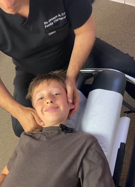 Dr. Joseph A. Cucci performing a gentle pediatric neck adjustment on a smiling child at his Family Chiropractic clinic in New York, NY.